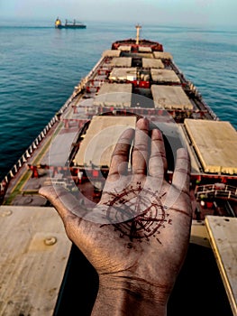 A sailor tattood compass on his hand and showing in the background of a ship