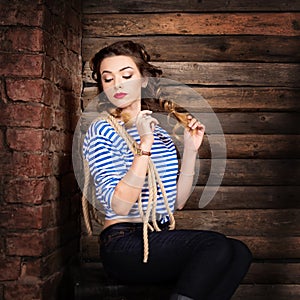 Sailor woman in striped vest and rope sitting on dower chest. wooden background