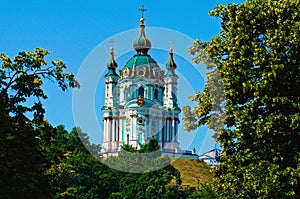 Saint Andrew`s Church on the top of the green hill. Tree leaves border. Natural frame. Blue sky background