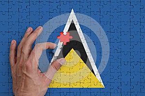 Saint Lucia flag is depicted on a puzzle, which the man`s hand completes to fold