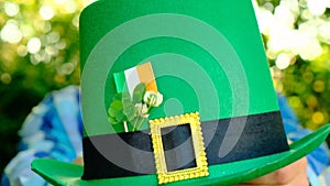 Saint Patrick festive .Close-up of a green hat in the hand of a man in a sunny spring garden.Four-leaf clover. Good luck