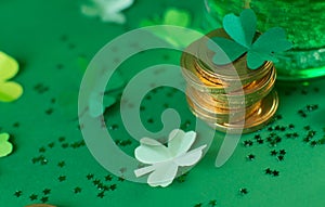Saint Patricks day backdrop with bear cup with ale, stack of chocolate coins, green four-leafed paper shamrocks
