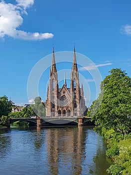 Saint Paul`s Church in Strasbourg surrounded by green trees and reflecting in the canal ater on a sunny summer day, Alsace, Franc