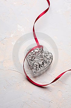 Saint Valentine day greeting card, beautiful silver heart with red ribbon on grey texture