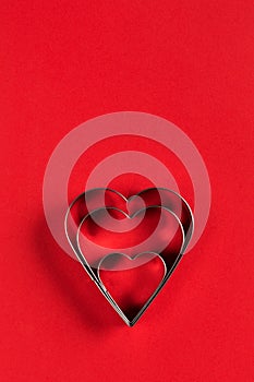 Saint Valentine day minimalistic greeting card, heart-shaped cookie cutters on red background with beautiful shadows