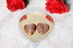 Saint valentine`s day concept: two chocolate  and red roses hearts rest on a marble table with copy space for your text