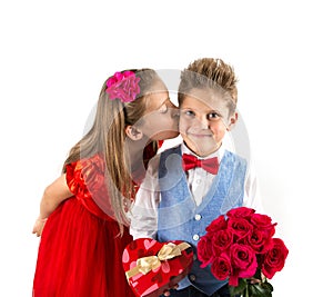 Saint Valentine`s day. Pretty girl with red dress and gentleman boy with blue vest, red butterfly tie, red roses bucket and heart
