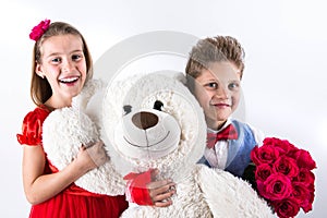 Saint Valentine`s day. Pretty girl with red dress and gentleman boy with blue vest, red butterfly tie, red roses bucket and heart