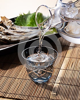 Sake poured into a faceted glass and grilled umeshi sardines placed behind it