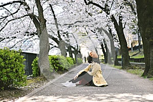 Sakura cherry blossoms full blooming, Asian smiling woman traveler sitting under the pink flower tree.