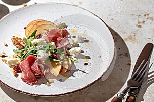 Salad of arugula and prosciutto with addition of sliced apple, cheese, walnuts and spices on a plate with cutlery cloe