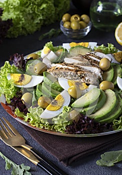 Salad with avocado, chicken, eggs and olives, dressed from lemon and olive oil, served on lettuce leaves on gray