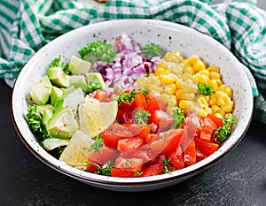 Salad with avocado, tomatoes, red onions and sweet corn in bowl.