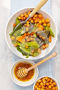 Salad with baked pumpkin and chickpeas with mustard-honey dressing in a white plate, top view. Healthy vegan food concept.