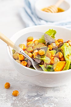 Salad with baked pumpkin and chickpeas with mustard-honey dressing in a white plate, macro. Healthy vegan food concept.