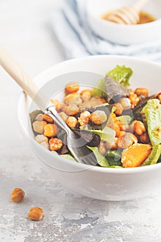 Salad with baked pumpkin and chickpeas with mustard-honey dressing in a white plate, macro. Healthy vegan food concept.