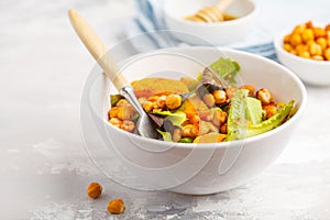 Salad with baked pumpkin and chickpeas with mustard-honey dressing in a white plate, macro. Healthy vegan food concept.