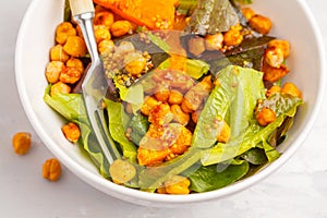 Salad with baked pumpkin and chickpeas with mustard-honey dressing in a white plate, macro. Healthy vegan food concept.