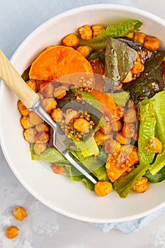 Salad with baked pumpkin and chickpeas with mustard-honey dressing in a white plate, top view. Healthy vegan food concept.