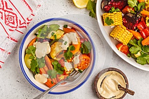 Salad with baked vegetables with tahini in white plate, white ba