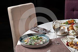 Salad with basil, cheese, fish. There are other dishes in the background. The table is set in a retoran.