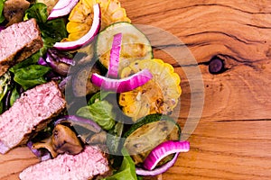 Salad with beef slices, grilled vegetables - eggplant, corn, mushrooms, sauce on a wooden board, dish