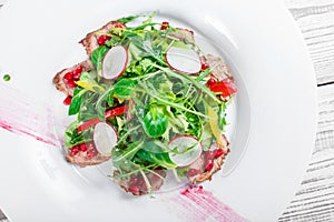 Salad with beef steak, baby spinach, lettuce, sweet pepper and grains of pomegranate on wooden background