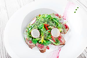 Salad with beef steak, baby spinach, lettuce, sweet pepper and grains of pomegranate on wooden background