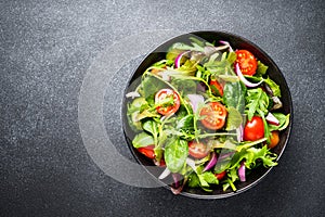 Salad in black bowl at dark background.