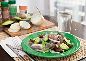 Salad of black tomatoes, avocado and onions on green plate