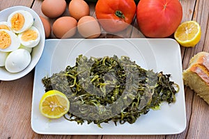 salad with boiled wild greens, dandelion, lemons and extra virgin olive oil, on a wooden table