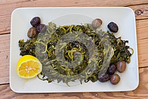 salad with boiled wild greens, dandelion, lemons and extra virgin olive oil, on a wooden table