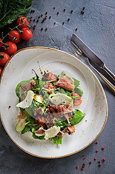 Salad with burrata, parma and cherry tomatoes confit. Spoon and a fork on the grey background