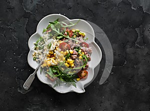 Salad with canned tuna, boiled egg, arugula, cherry tomatoes and corn on a dark background, top view