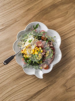 Salad with canned tuna, boiled egg, arugula, cherry tomatoes and corn on a wooden background, top view