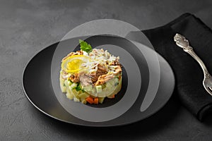 Salad with canned tuna and vegetables in culinary ring on black plate.