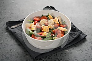 Salad with cherry tomatoes, mixed grens and cheese in white bowl on concrete background