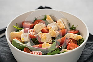 Salad with cherry tomatoes, mixed grens and cheese in white bowl on concrete background