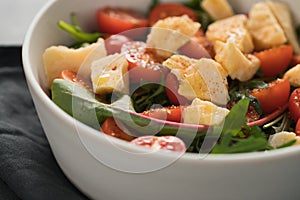 Salad with cherry tomatoes, mixed grens and cheese in white bowl on concrete background