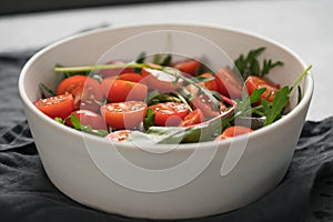 Salad with cherry tomatoes and mixed grens in white bowl on concrete background