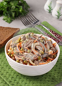 Salad with chicken hearts, canned peas, onions and carrots in a white bowl