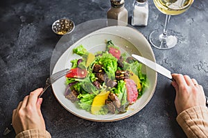 Salad with citrus, lettuce and grilled chicken liver in a plate and feminine hand.