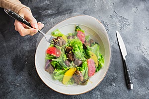 Salad with citrus, lettuce and grilled chicken liver in a plate and feminine hand