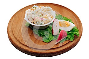 Salad with crab sticks, cubed cucumber, corn and egg with mayonnaise on a board isolated on a white background.