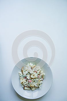 Salad with crackers, crab sticks, chicken fillet, fresh greens and hard cheese, seasoned with mayonnaise oil, served in a white