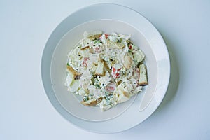 Salad with crackers, crab sticks, chicken fillet, fresh herbs and hard cheese seasoned with mayonnaise butter served in a white