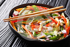 Salad of cucumbers, peppers, carrots, pea pods with sesame and peanuts close-up on a plate. horizontal