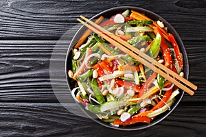 Salad of cucumbers, peppers, carrots, pea pods with sesame and peanuts close-up on a plate. horizontal top view