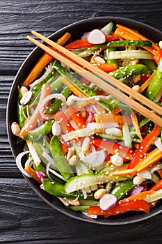 Salad of cucumbers, peppers, carrots, pea pods with sesame and peanuts close-up on a plate. Vertical top view