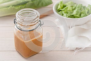 Salad dressing in a glass container on light wooden background